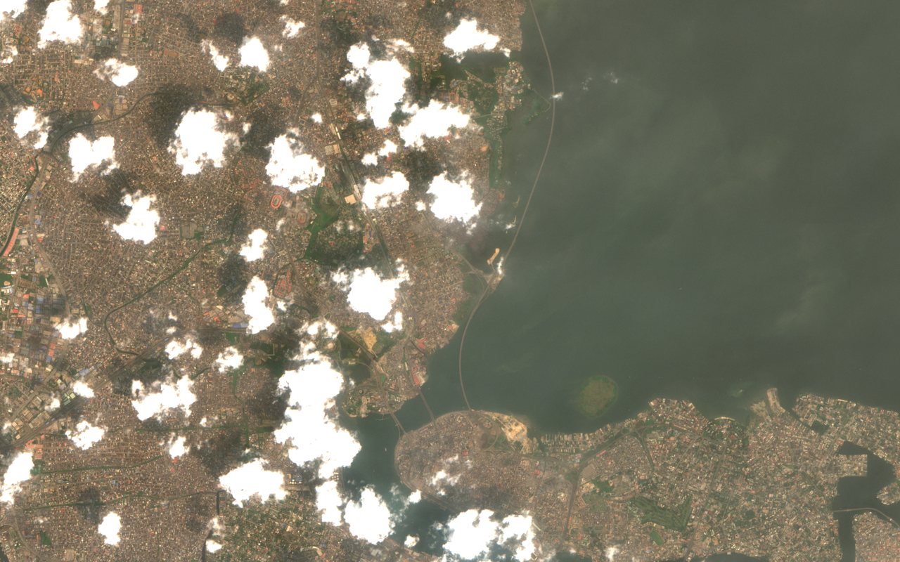 Sentinel-2 true-colour view of Lagos, Nigeria, on 24 January 2026: a very dense built-up area beside the dark green-brown Lagos Lagoon, long bridges crossing the water and a few small white clouds with dark shadows.